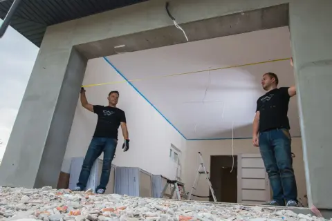 Dwóch mężczyzn mierzy otwór bramy garażowej. Precyzyjna obróbka otworu to klucz do idealnego montażu.