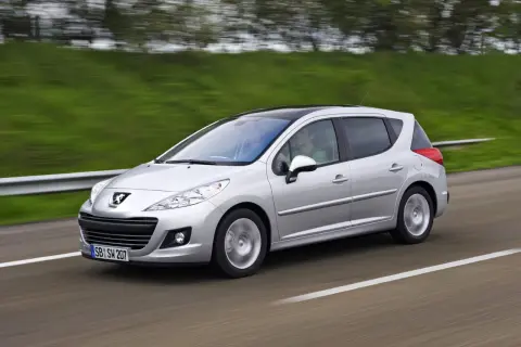 Srebrny Peugeot 207 1.6 HDI z czarnym dachem pędzi po drodze, za kierownicą siedzi mężczyzna, a obok niego pasażerka.