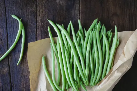 Fagiolini freschi pronti per essere bolliti in acqua fredda o calda, disposti su carta da forno su un tavolo di legno scuro.