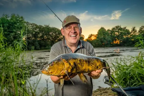 Glücklicher Angler hält großen Fisch am Lohheider See im Abendlicht.