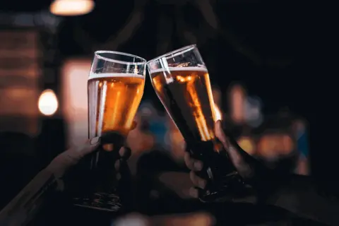Due mani brindano con due bicchieri di birra dorata, un gesto che nasconde un'intolleranza alla birra.