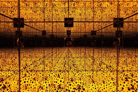 A dazzling infinity room with crystal bridges, bathed in golden light and adorned with Yayoi Kusama's iconic polka dots, creating an endless, mesmerizing spectacle.