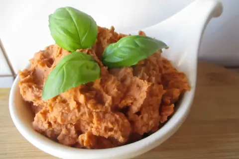 Pyszna pasta z białej fasoli, doprawiona ziołami i udekorowana listkami bazylii, podana w białej miseczce.