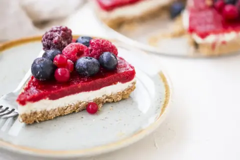 Una fetta di cheesecake ai frutti di bosco, con una glassa rossa brillante e bacche fresche, su un piatto con una forchetta.