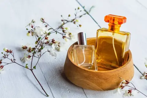Dwie buteleczki perfum, jedna w szkle, druga w bursztynowym kolorze, w drewnianej miseczce, otoczone delikatnymi kwiatami. Czy to woda toaletowa czy tester?