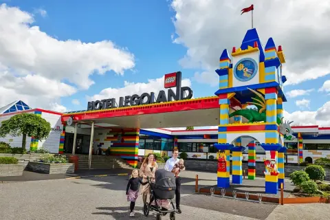 Rodzina z wózkiem spacerowym przed kolorowym hotelem Legoland Kopenhaga. Smoczy zegar i wejście z klocków LEGO.