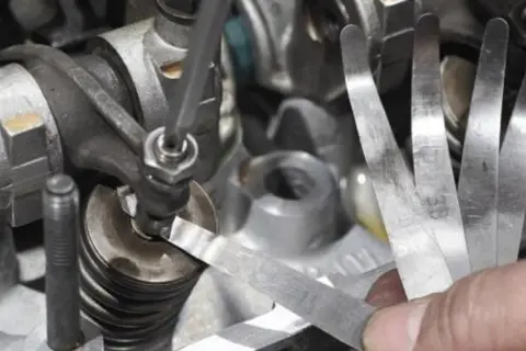 Precyzyjna regulacja zaworów silnika przy użyciu szczelinomierza. Mechanik sprawdza luz zaworowy.