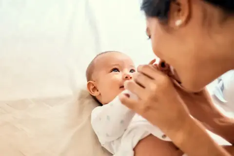 Uśmiechnięte dziecko reaguje na imię, gdy mama pochyla się, by je pocałować.