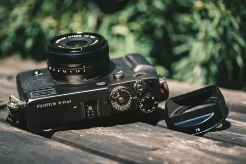 A Fujifilm X-Pro3 camera with a lens and lens hood rests on a wooden surface, ready for a photography review.