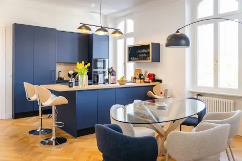 Une belle idée cuisine ouverte sur salon avec des meubles bleus profonds, un îlot central et une table en verre.
