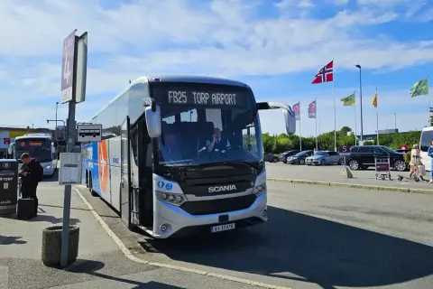 Autobus FB25 Torp Airport czeka na pasażerów. W tle parking i norweskie flagi.