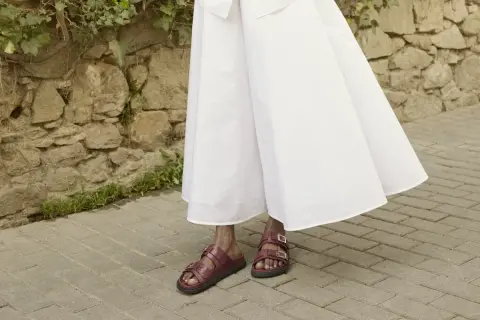 Czerwone sandałki na płaskiej podeszwie idealnie pasują do zwiewnej, białej sukienki. Oto inspiracja, jakie buty do eleganckiej sukienki wybrać na co dzień.
