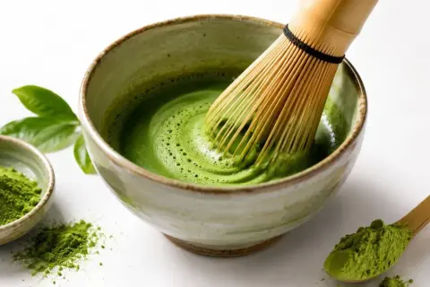 Przygotowanie idealnego naparu matcha: zielony proszek, bambusowa miotełka i miseczka z pianką.