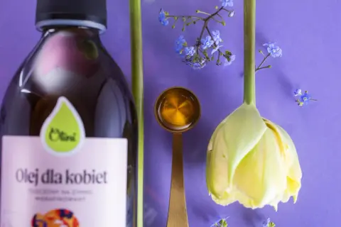 Olej dla kobiet i kwiaty symbolizują naturalne sposoby na menopauzę. Złota łyżeczka z płynem sugeruje wsparcie w tym okresie.