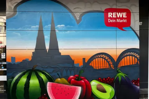 Graffiti mit Kölner Dom, Brücke und Früchten vor REWE-Logo.