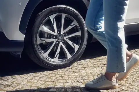 Osoba w jeansach i białych butach zbliża się do Toyoty Corolli. Dowiedz się, jak zresetować czujnik ciśnienia w oponach w tym modelu.