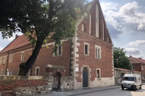 Stary ceglany budynek z kamiennymi detalami, otoczony murem i drzewem. To jedna z kazimierza wielka atrakcji, gdzie historia spotyka się z teraźniejszością.