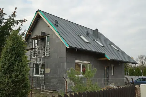 Trwa remont starego domu. Szara bryła z nowym dachem, oknami i rusztowaniami czeka na wykończenie.