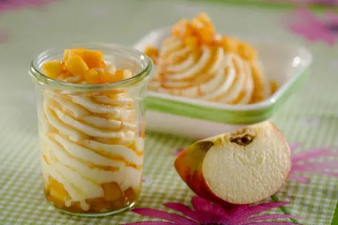 Cremige Mehlspeise mit Apfelstücken in einem Glas, daneben eine Schüssel mit derselben Leckerei und ein Apfelstück.