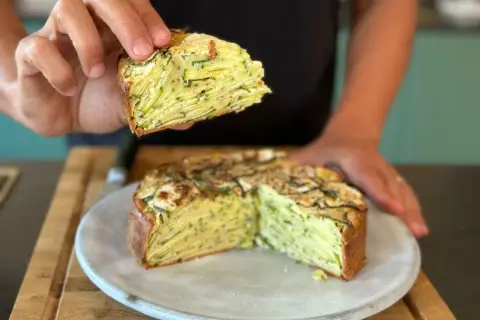 Une main tient une part d'un gâteau aux courgettes, révélant ses fines couches. Ce délice est presque invisible aux courgettes, tant elles sont bien intégrées.