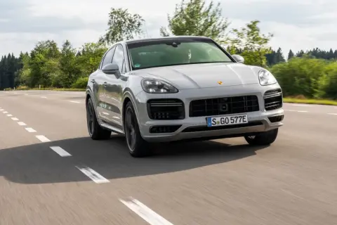 Srebrny Porsche Cayenne 2025 sunie po asfaltowej drodze, otoczony zielenią lasów.
