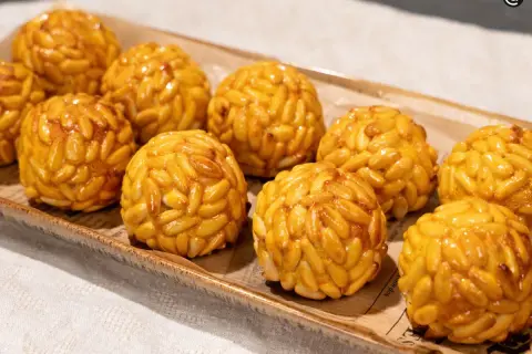 Panellets de boniato cubiertos de piñones dorados, presentados en una bandeja rústica.