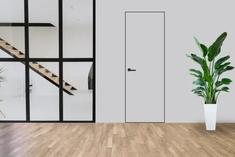Minimalistyczne wnętrze z widocznymi schodami za szklaną ścianą i dyskretnymi drzwiami ukrytymi w ścianie. Obok stoi duża roślina w białej donicy.