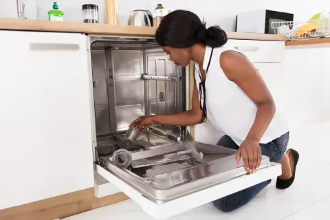A woman is kneeling and placing a filter into a new dishwasher during its installation.