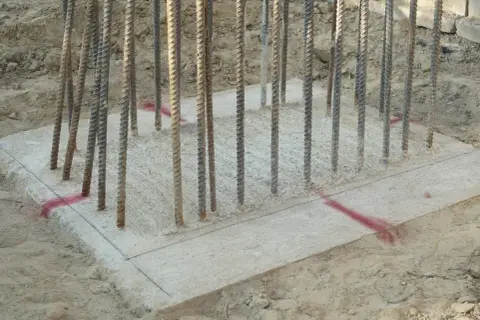 Zbrojenie fundamentów pod budowę altany ogrodowej. Betonowa płyta z wystającymi prętami, gotowa na dalsze prace.