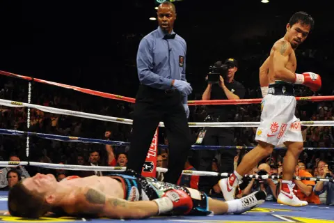 A boxer lies on the canvas as the referee stands over him. The victor, Manny Pacquiao, walks away, his red glove raised. Can you push in boxing? Yes, this is the result of a powerful punch.
