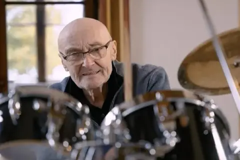 Phil Collins, legenda perkusji, siedzi przy zestawie bębnów, gotów do gry.