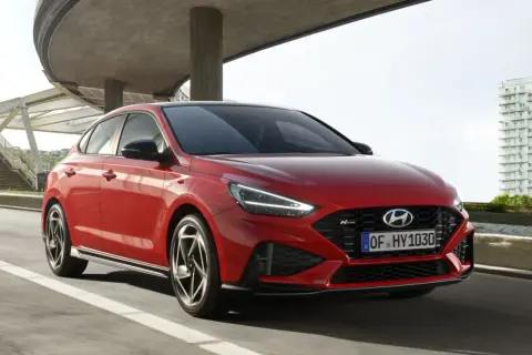 Czerwony Hyundai i30 hatchback N Line w ruchu miejskim, z nowoczesną architekturą w tle.