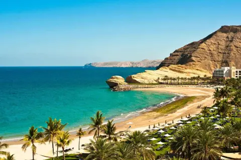 Traumhafte Bucht mit Palmen, Sandstrand und Felsen. Ein Hotel am Hang. Perfekt für Oman Reisetipps.