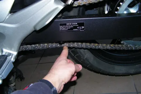 Sprawdzanie naciągu łańcucha w motocyklu. Palec pokazuje luźny łańcuch napędowy.