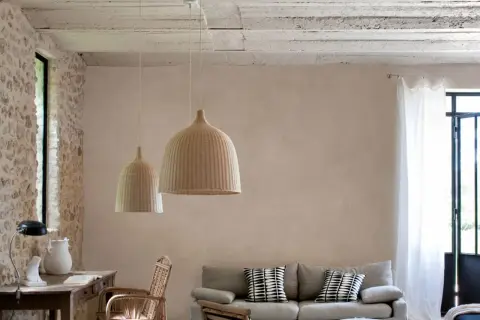Un salon lumineux avec un mur en enduit mur interieur texturé, des suspensions en rotin, un canapé et des meubles en bois.