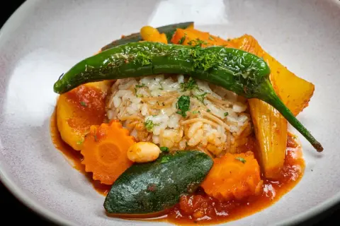 Herzhaftes Reisgericht mit viel Gemüse, darunter Karotten, Zucchini und eine grüne Chilischote, serviert in einer roten Sauce.