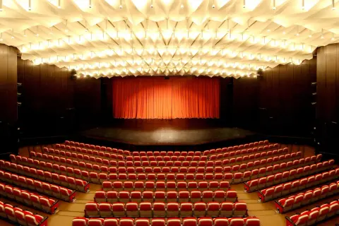 Leere rote Sitze im **Theater und Konzerthaus Solingen** warten auf Besucher. Die Bühne ist mit einem roten Vorhang verdeckt.