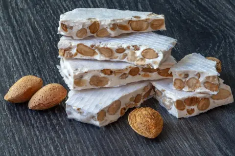 Barras de turrón, un dulce tradicional español, apiladas con almendras enteras. ¿Qué es nougat? Es este delicioso manjar.