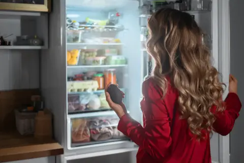 Kobieta w czerwonej piżamie trzyma awokado, zastanawiając się, na ile stopni ustawić lodówkę i zamrażarkę, by zachować świeżość produktów.