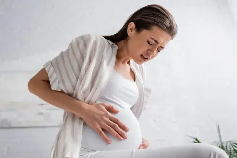 Kobieta w ciąży z wyrazem bólu na twarzy trzyma się za brzuch. To może być ból brzucha na początku ciąży.