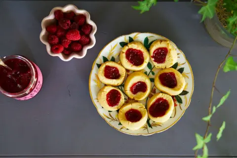Hallongrottor recept: småkakor med hallonsylt på en vacker tallrik, bredvid en skål med färska hallon och en burk sylt.