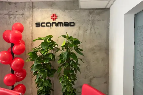 Czerwone balony i logo "Scanmed" na betonowej ścianie, obok zielonych roślin.