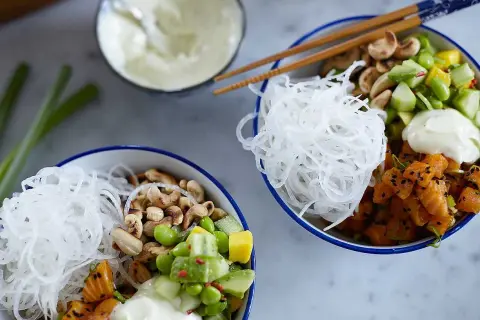 Två färgglada pokebowls med lax, grönsaker, nötter och risnudlar. Ett perfekt pokebowl recept för en hälsosam lunch.