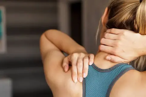 Une femme se masse le cou et les épaules, cherchant un soulagement pour ses trapezes tendus.