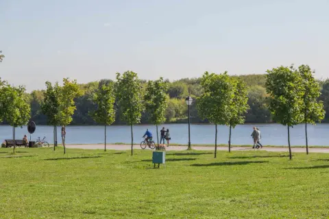 Spacer po alejkach nad zalewem nowohuckim. Ludzie spacerują, jeżdżą na rowerze, ciesząc się słońcem i zielenią.