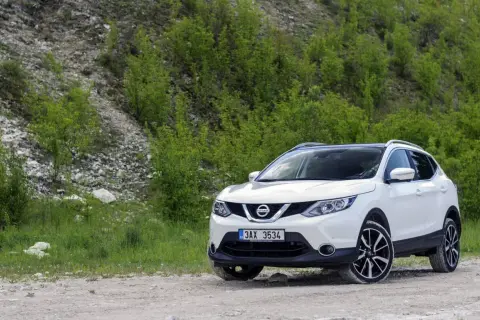 Biały Nissan Qashqai J11 na drodze szutrowej, otoczony zielenią i kamienistym zboczem.