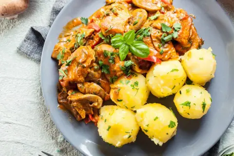 Pyszny gulasz z indyka z pieczarkami i papryką, podany z kluskami śląskimi posypanymi natką pietruszki.