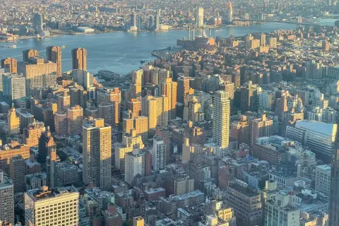 Widok z lotu ptaka na Manhattan i Brooklyn o zachodzie słońca. Rzeka Hudson rozdziela dwa miasta, a światła miasta zaczynają migotać.
