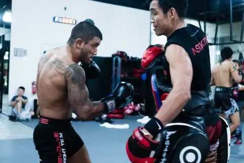Boxers train in a gym. One boxer throws a punch, possibly an uppercut, as the other defends with pads.