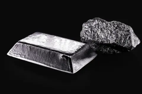 Sztabka i bryła platyny, najdroższego metalu na świecie, lśnią na czarnym tle.